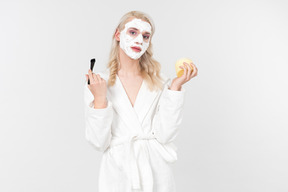 A good looking blond-haired young man in a white bathrobe, being in the process of his beauty care routine