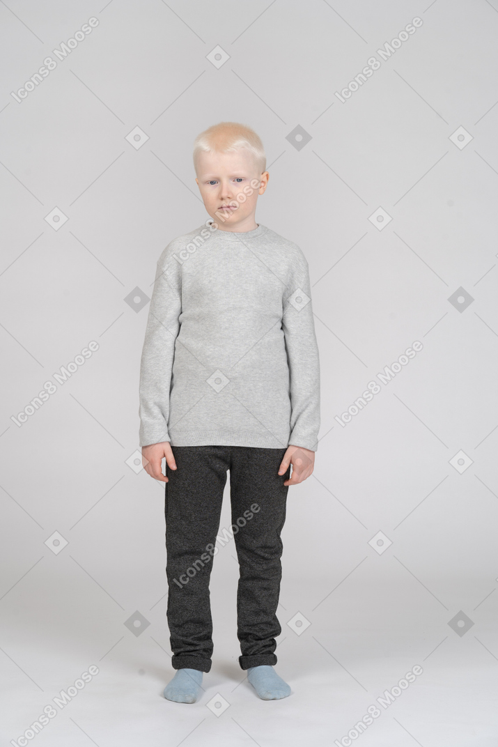 Front view of a sad kid boy standing still and looking aside