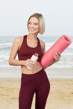 A woman holding a pink yoga mat and a bottle of water