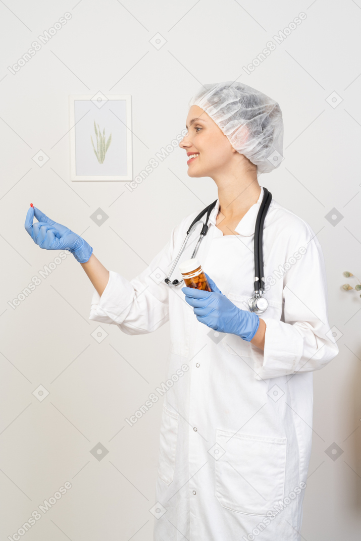 Side view of a smiling young female doctor offering a pill