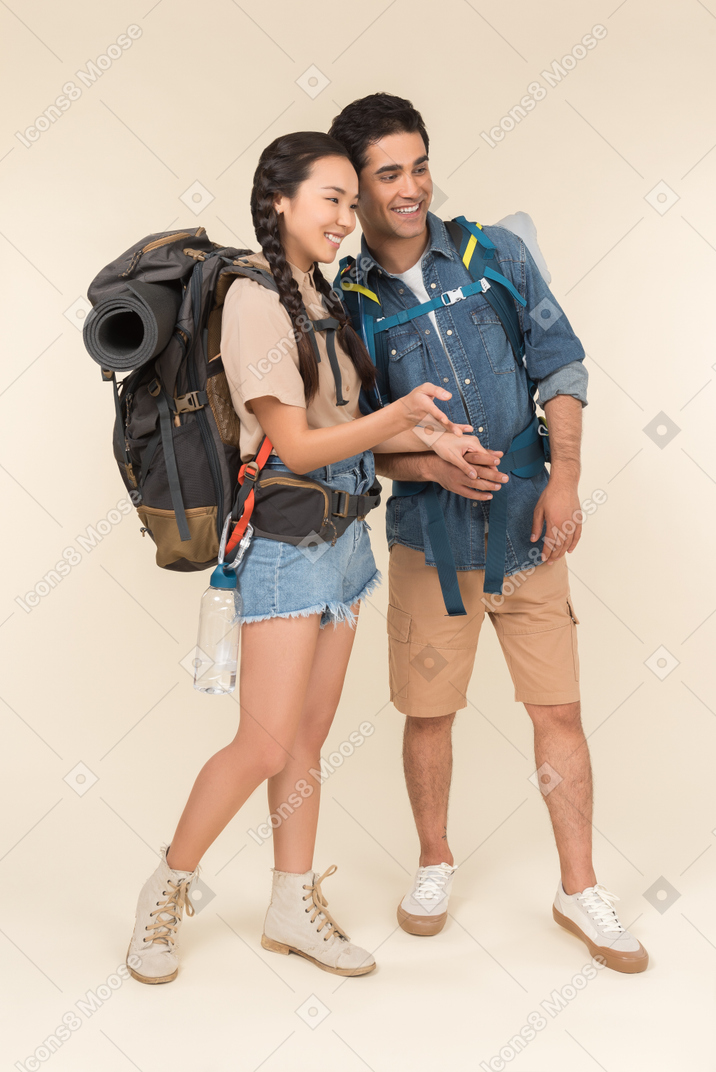 Jovem mulher asiática com mochila enorme mostrando algo para seu namorado