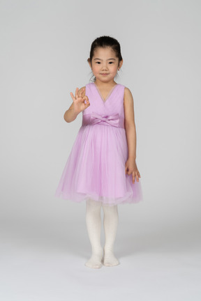 Portrait en pied d'une petite fille faisant signe ok