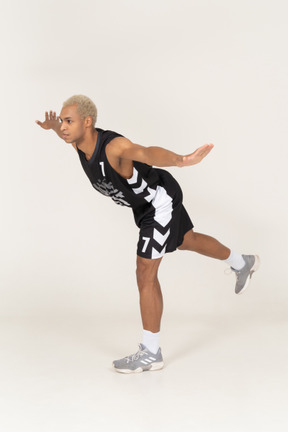 Three-quarter view of a balancing young male basketball player leaning forward & standing on one leg