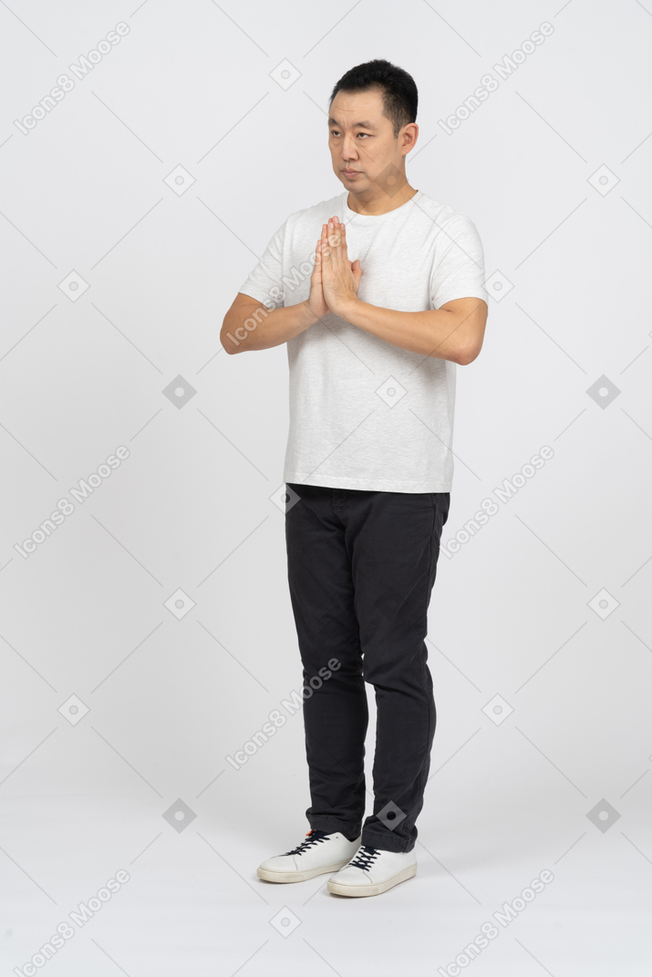 Three-quarter view of a man in casual clothes making praying gesture