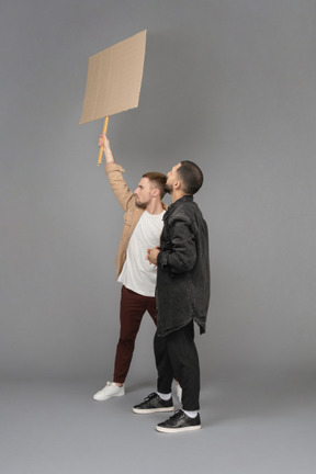 Vista lateral de dos hombres jóvenes con una cartelera levantada