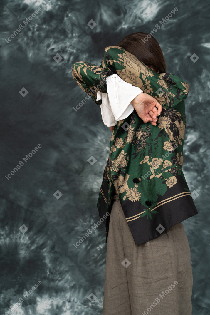 Three-quarter shot of young woman in silk jacket hiding her face