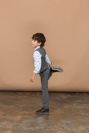 Vista lateral de um menino de terno cinza posando em uma perna