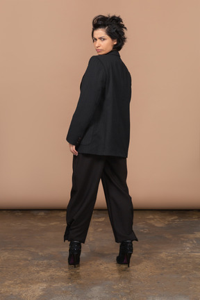 Vista posteriore di una donna d'affari che indossa sopracciglia maglieria abito nero e guardando la fotocamera