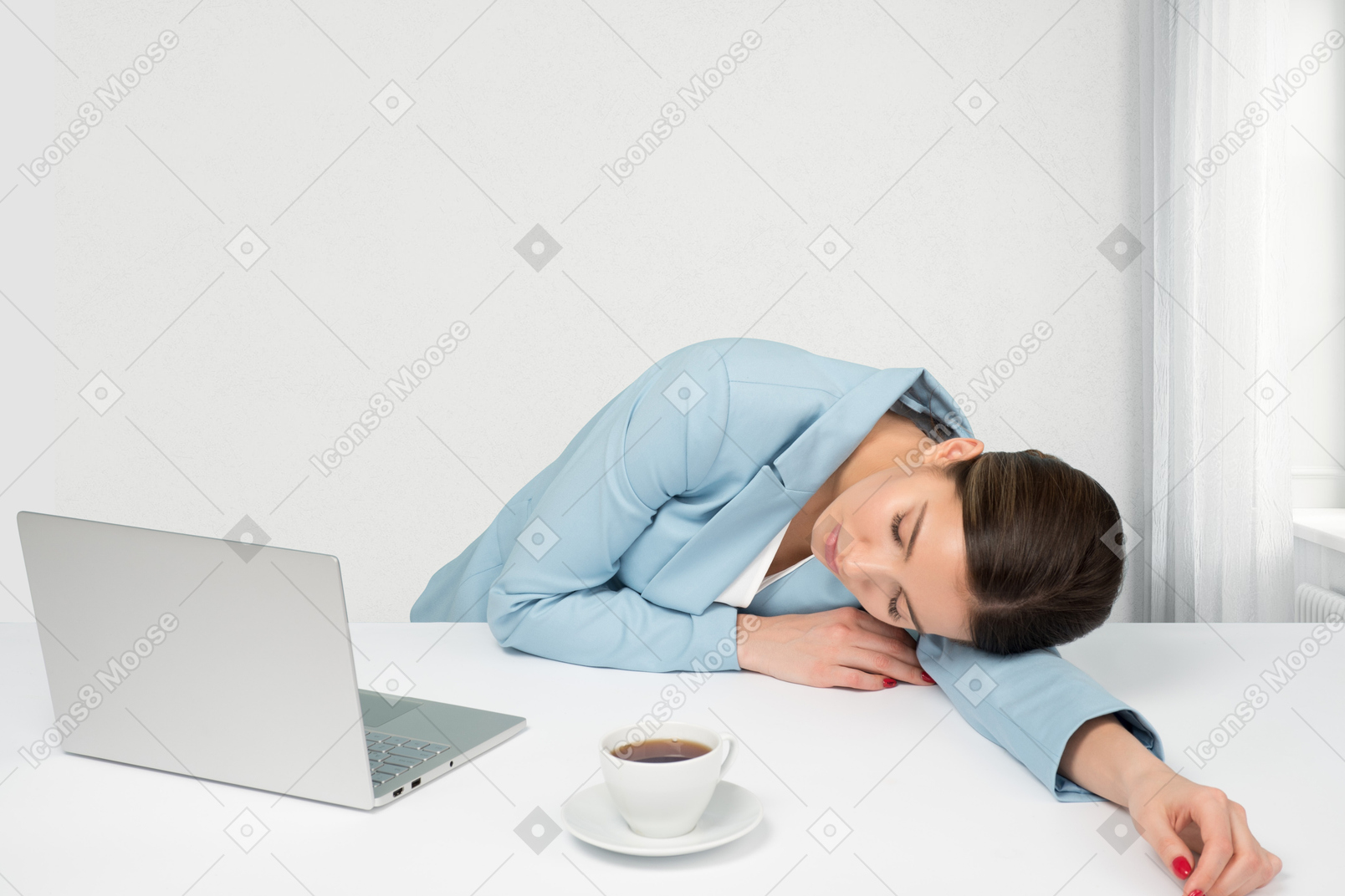 A woman laying her head on her desk next to a laptop