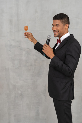Smiling young man with a mic and champagne glass talking