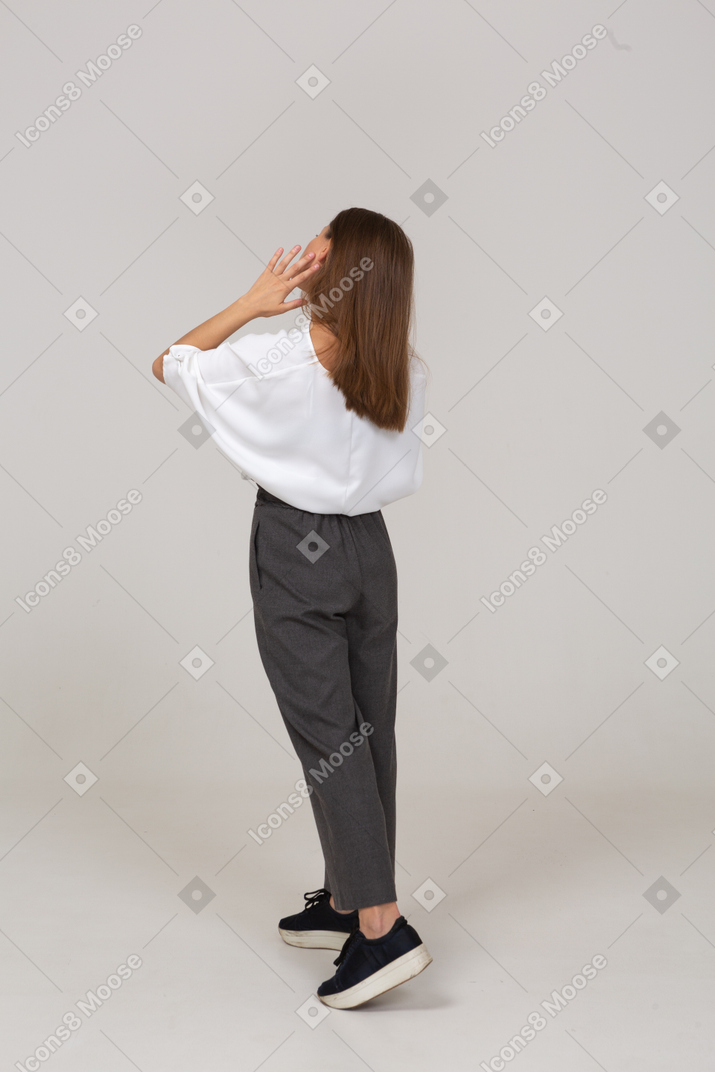 Three-quarter back view of a young lady in office clothing touching her face