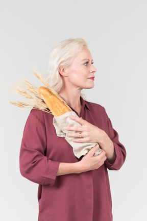 A nice-looking middle-aged blonde woman in a burgundy shirt and with a freshly bought bread in her hands