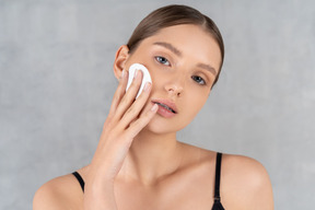 Attractive woman wiping her face with cotton pad