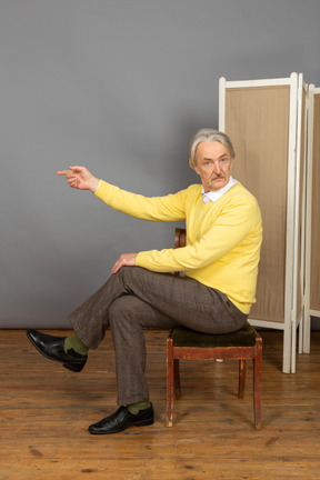 Hombre sentado en una silla y apuntando a la izquierda