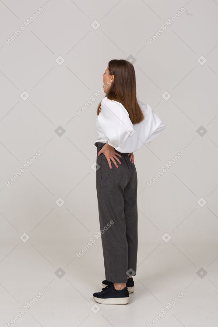 Three-quarter back view of a yawning young lady in office clothing putting hands on hips