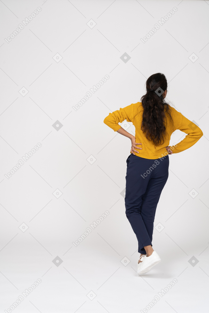腰に手を置いて歩くカジュアルな服装の女の子の背面図