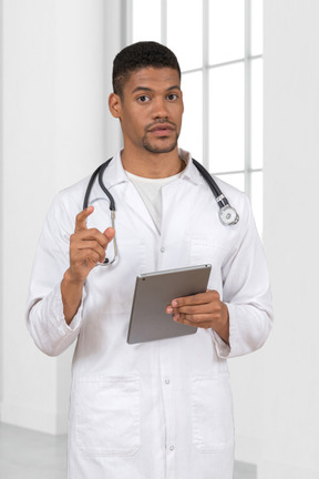 A man in a white lab coat pointing finger and holding a tablet