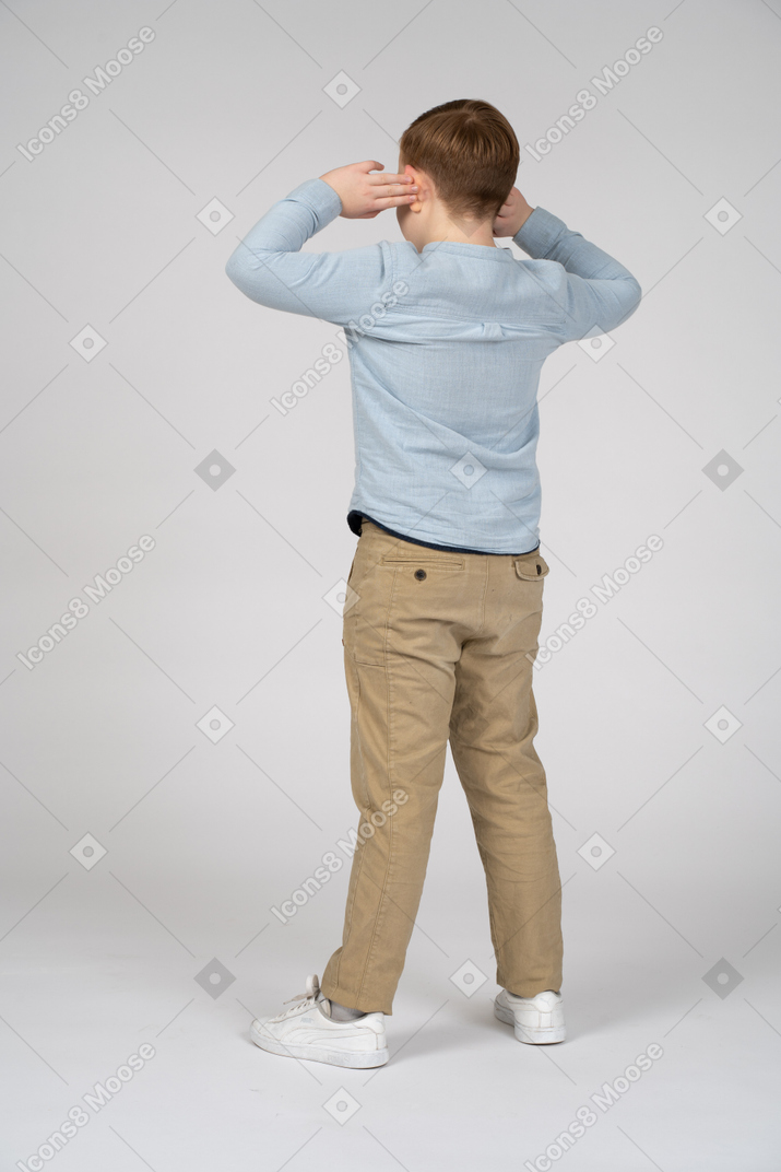 一个男孩双手放在头上站立的后视图