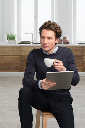 A man sitting on a stool holding a cup of coffee