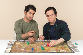 Two young interracial friends sitting at the table and playing board game