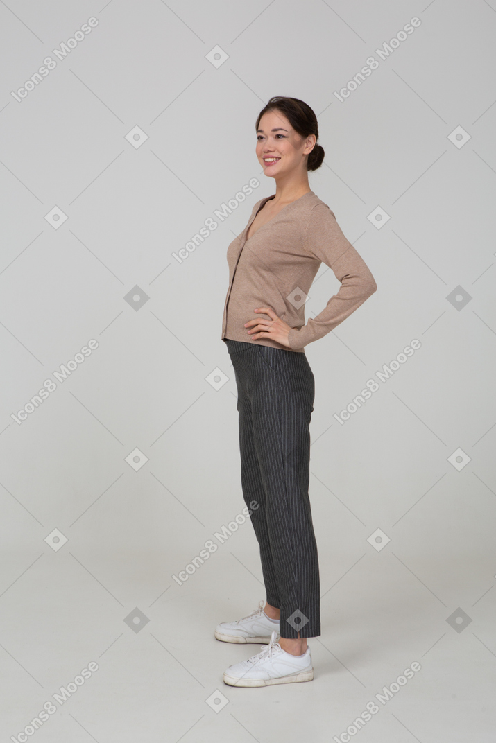 Vista de tres cuartos de una joven sonriente en jersey y pantalones poniendo las manos en las caderas