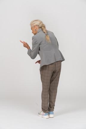 Vista trasera de una anciana en traje mostrando una señal de advertencia