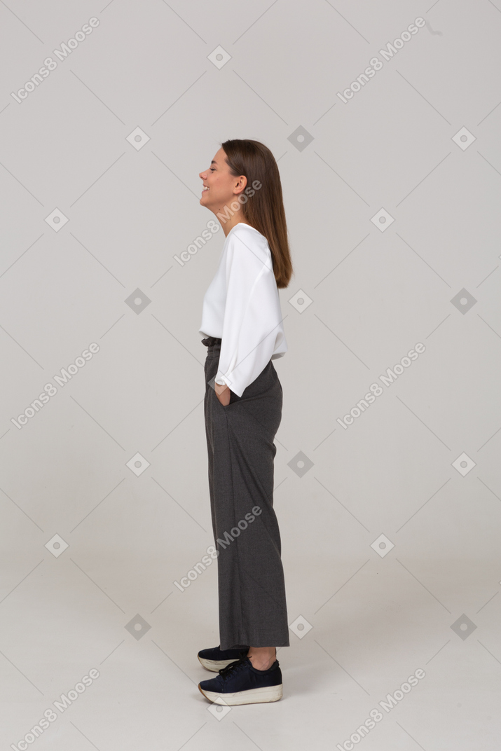 一个微笑的年轻女士在办公室服装把手放在口袋里的侧视图