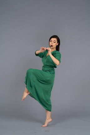 Side view of a dancing young lady in green dress playing flute