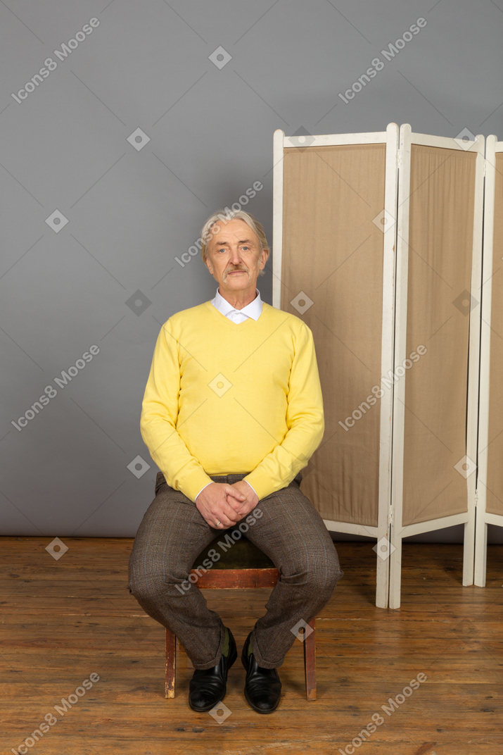 Man sitting on chair with hands clasped at his groin