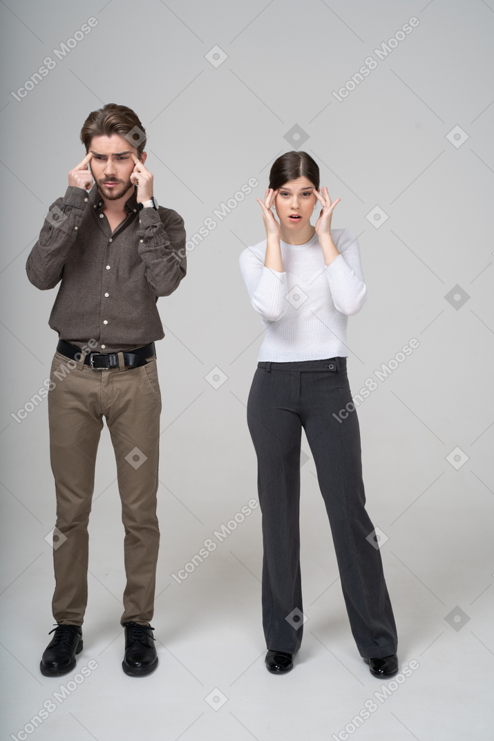 Front view of a young couple in office clothing touching face & narrowing eyes