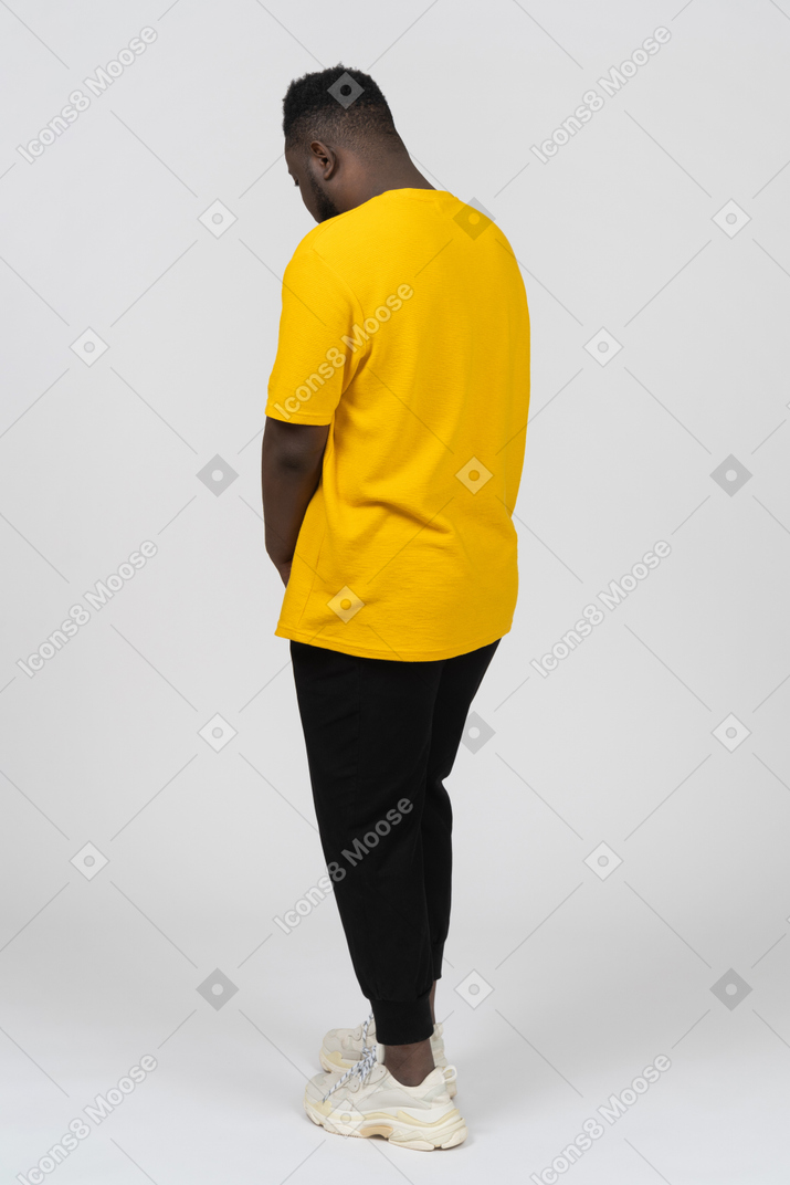 Dreiviertelansicht von hinten auf einen zurückgezogenen jungen dunkelhäutigen mann in gelbem t-shirt