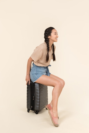 Smiling young female traveller sitting on suitcase