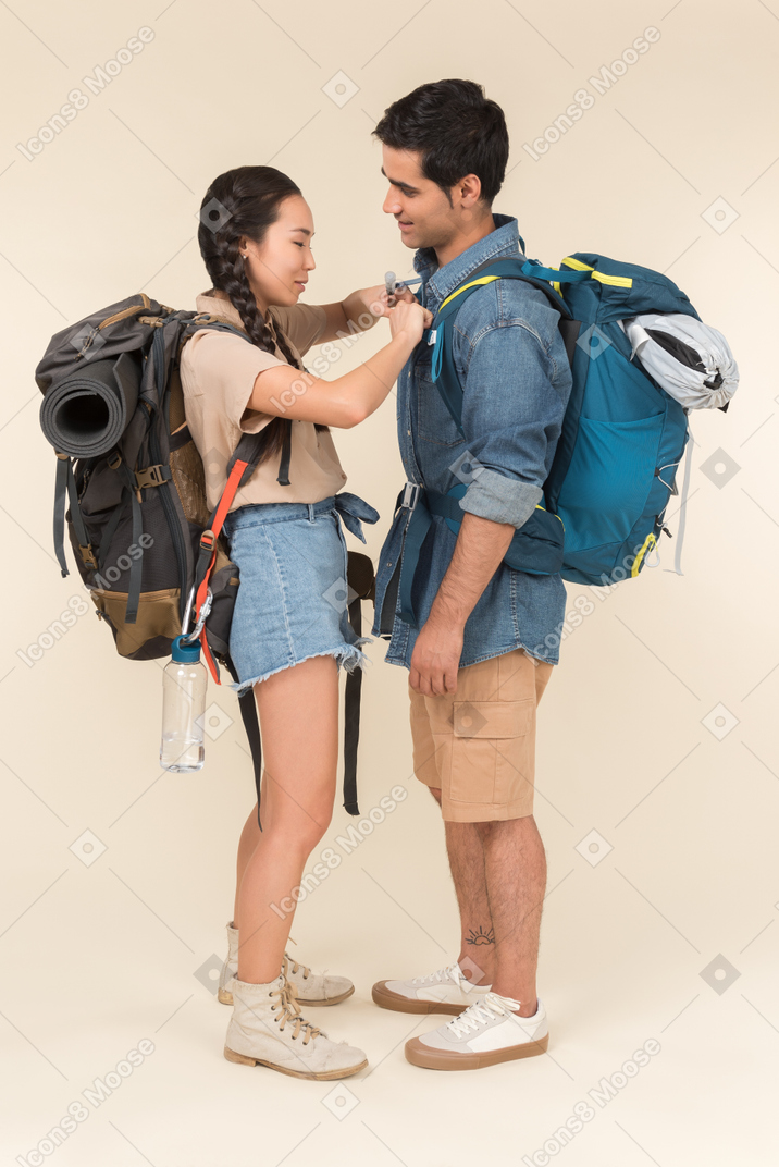 Riendo joven pareja interracial de pie cerca uno del otro con mochilas