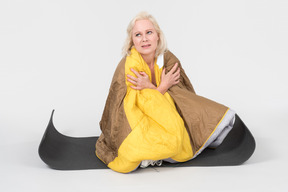 Mature woman sitting on yoga mat wrapped in blanket