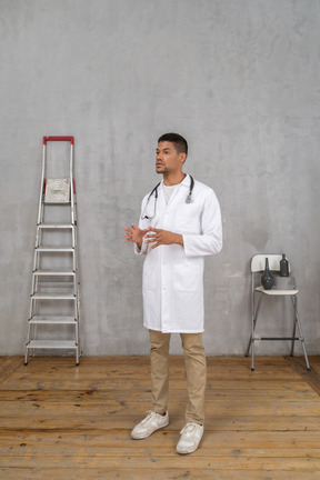 Vista de três quartos de um jovem médico em uma sala com escada e cadeira explicando algo
