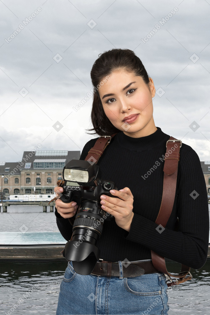A woman holding a camera in front of a body of water