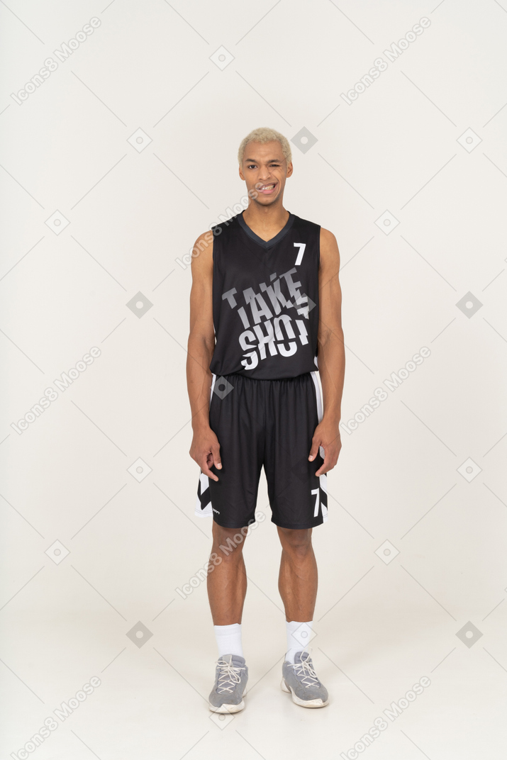 Vista frontal de um jovem jogador de basquete masculino a piscar e a sorrir, parado