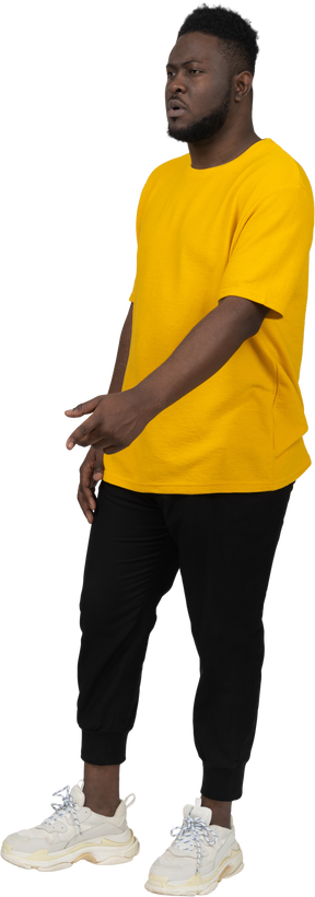 뭔가를 설명하는 노란색 티셔츠를 입은 몸짓을 하는 짙은 피부의 젊은 남자의 3/4 보기