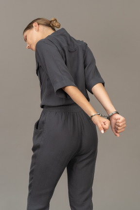 Three-quarter back view of a suffering young woman in a jumpsuit wearing handcuffs