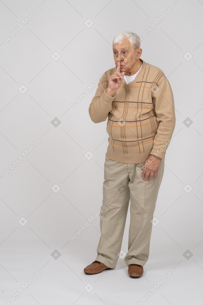 Front view of an old man in casual clothes making shhh gesture