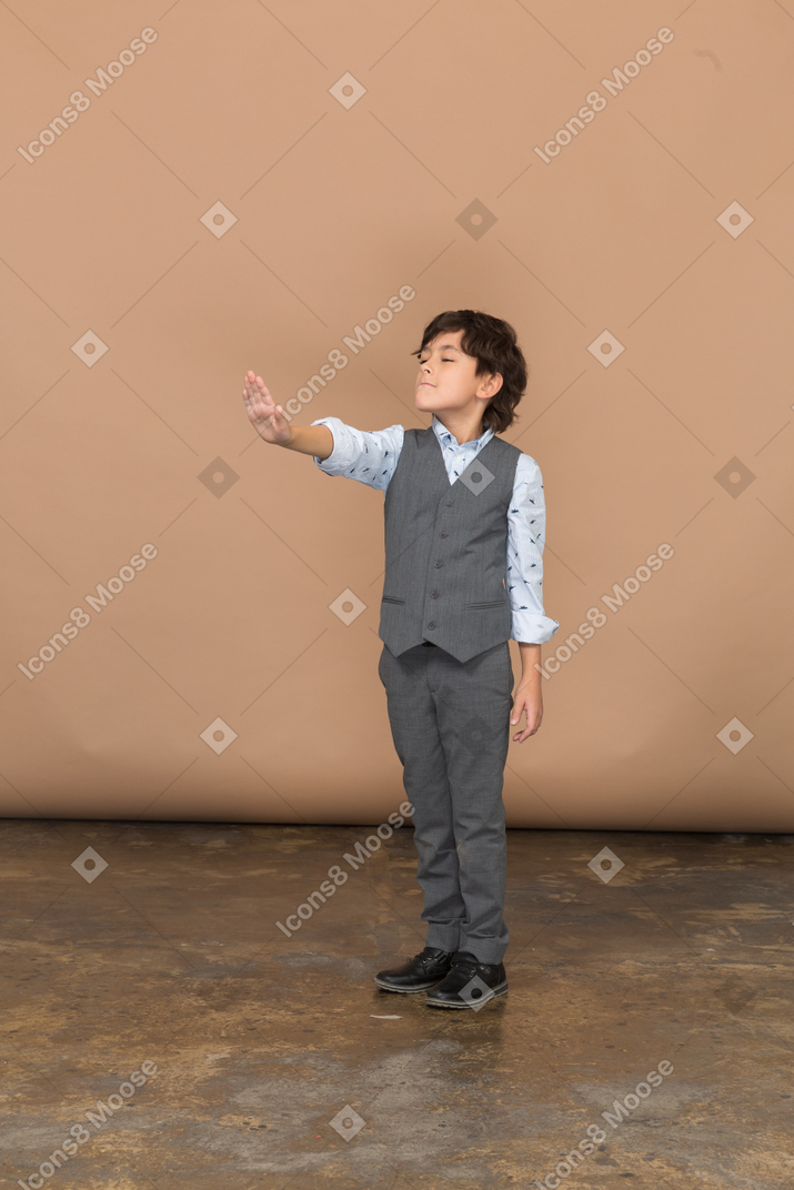 Front view of a cute boy in grey suit standing with outstretched arm