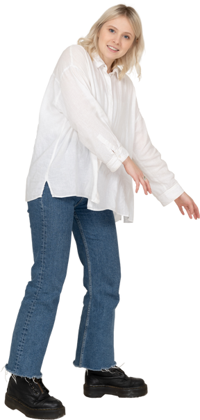 Vista di tre quarti di una donna bionda in abiti casual che si fa da parte mentre tende le mani e guarda la fotocamera