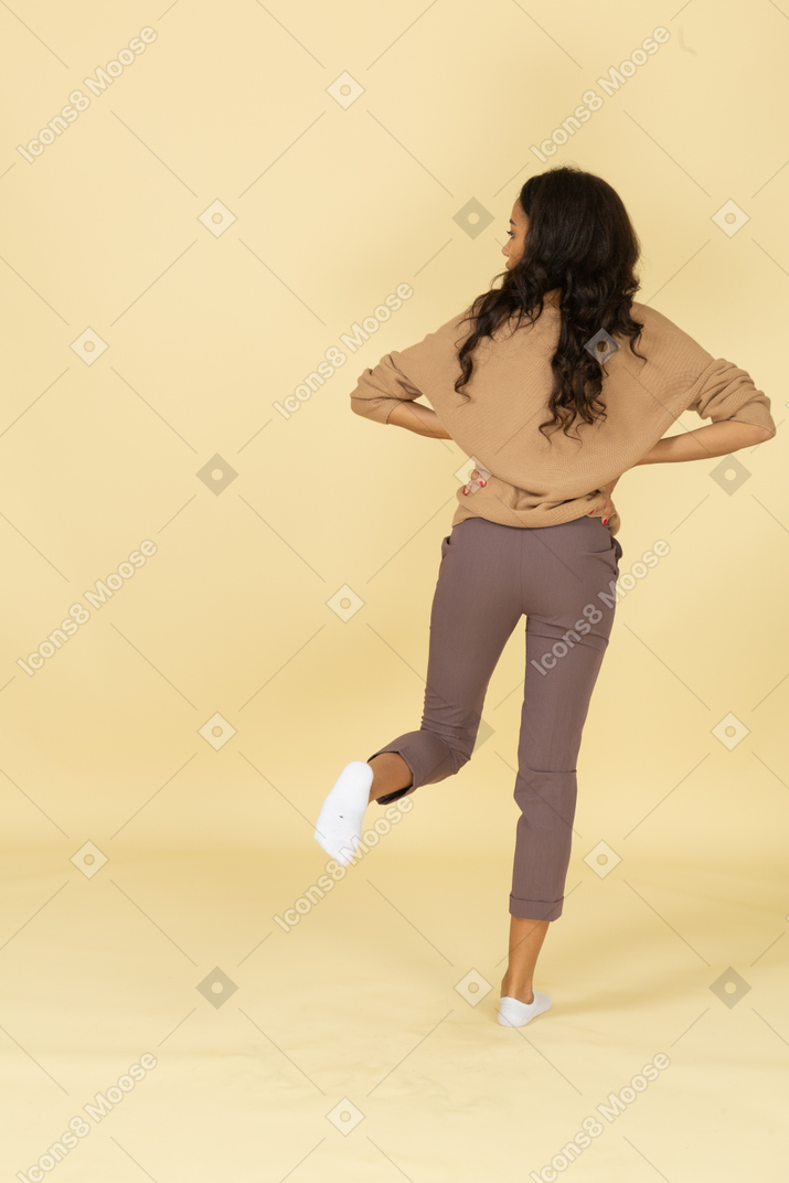 Vista posterior de una mujer joven de piel oscura poniendo las manos en las caderas mientras mira a un lado