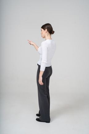 Вид сбоку молодой женщины в черных брюках и белой блузке, указывающей пальцем