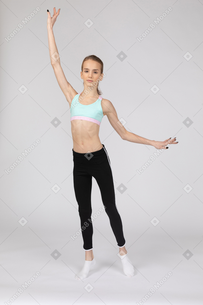 Front view of a teen girl in sportswear raising hands and putting her leg aside