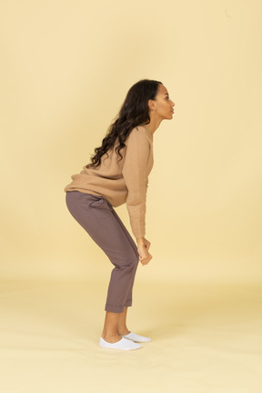 Vista lateral de una mujer joven de piel oscura levantando pesas