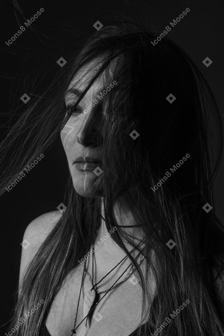Side view noir picture of a young female with face art looking aside with messy hair