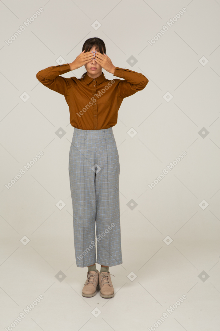 Vista frontale di una giovane donna asiatica in calzoni e camicetta che nasconde gli occhi