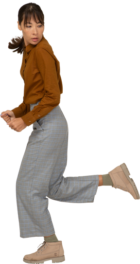 Vista lateral de uma jovem mulher asiática correndo de calça e blusa, virando-se