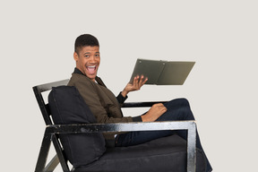 Seitenansicht eines jungen mannes, der auf einem sofa sitzt und einen laptop hält